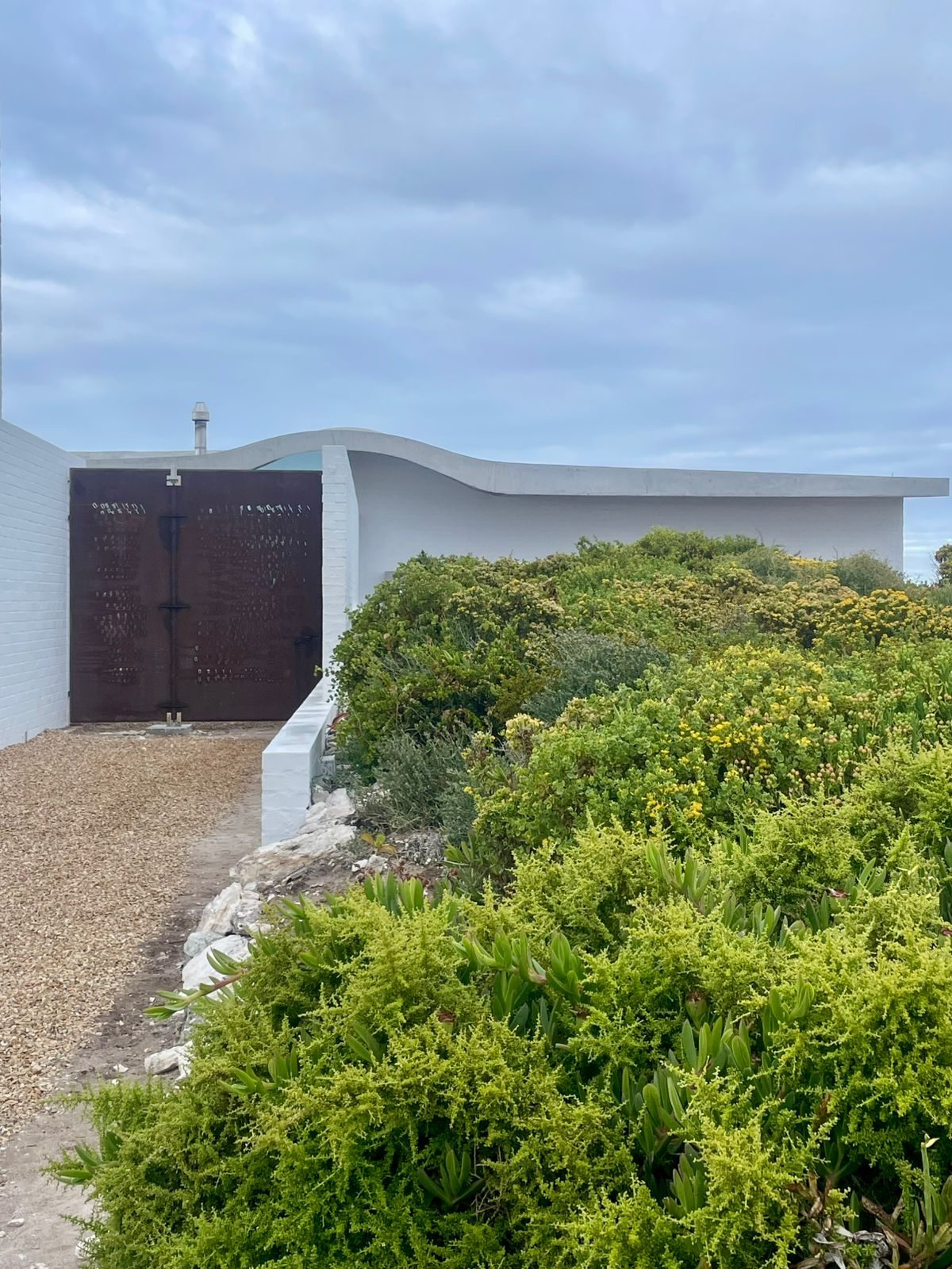 House Yzerfontein — concrete shell roof emerging from Strandveld fynbos, laser-cut entrance door